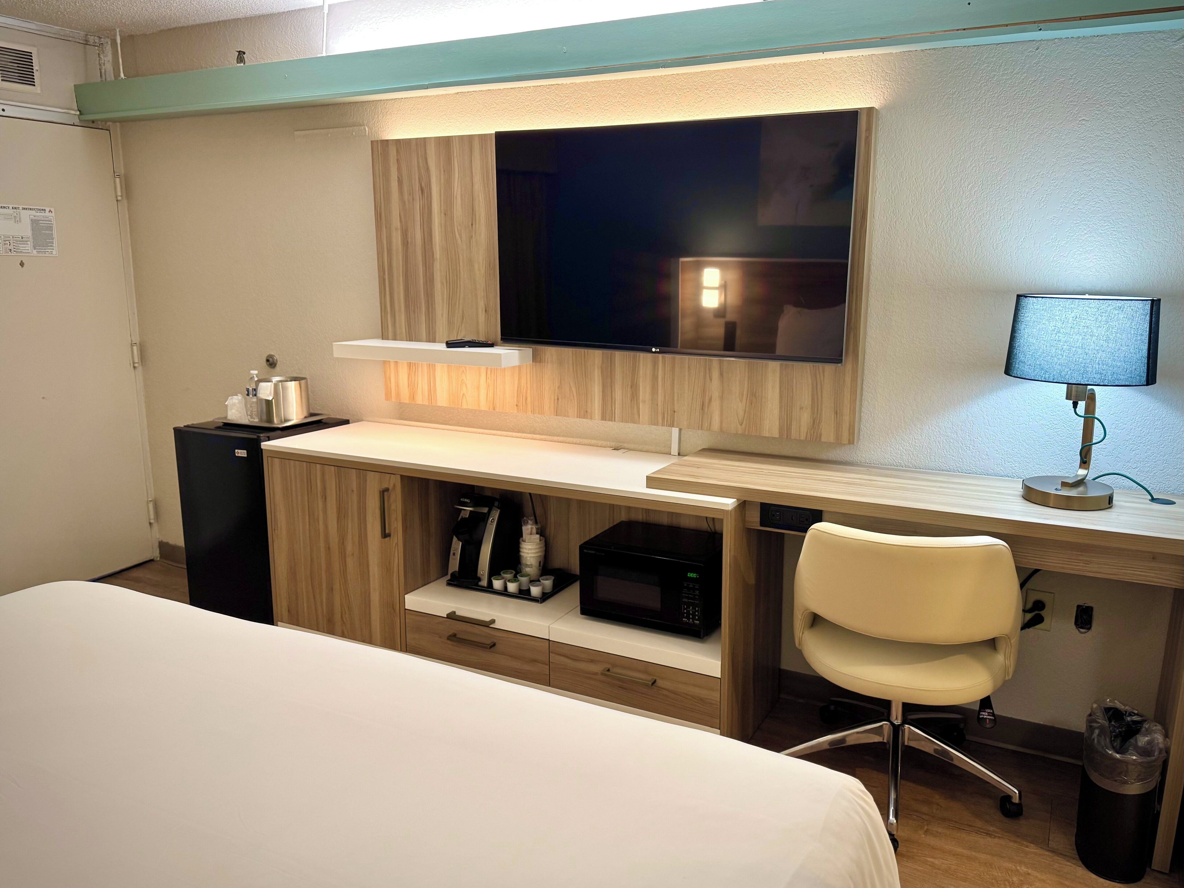 Habitación de hotel con cama, escritorio con computadora, silla, televisor y microondas.