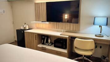 A hotel room with a bed, a desk with a computer, a chair, a TV, and a microwave.