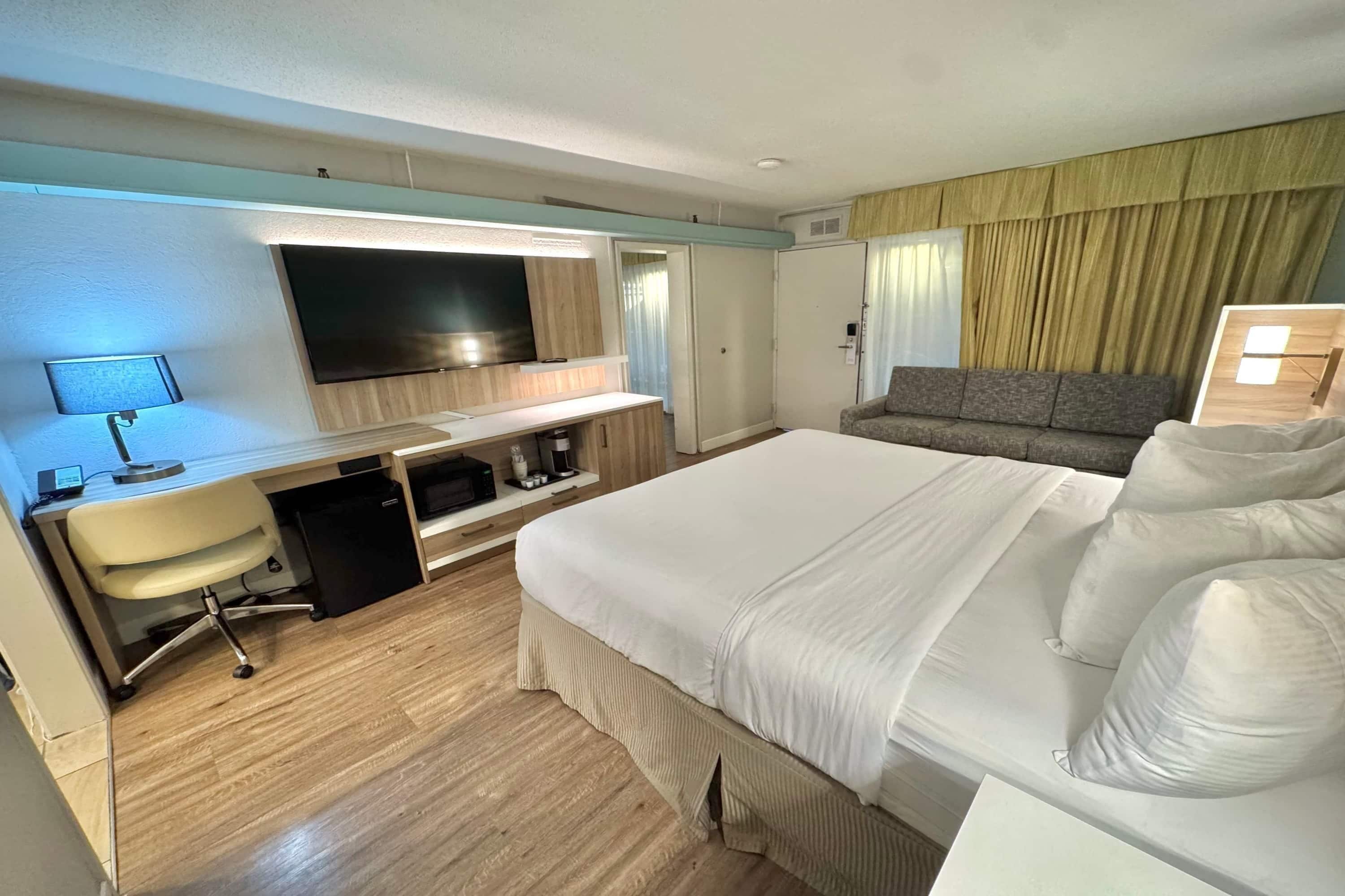 A hotel room with a bed, a desk with a computer, a TV, and a sofa.