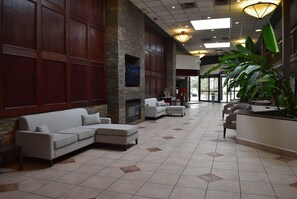 A spacious lobby with a sectional sofa, a fireplace, and a large plant.