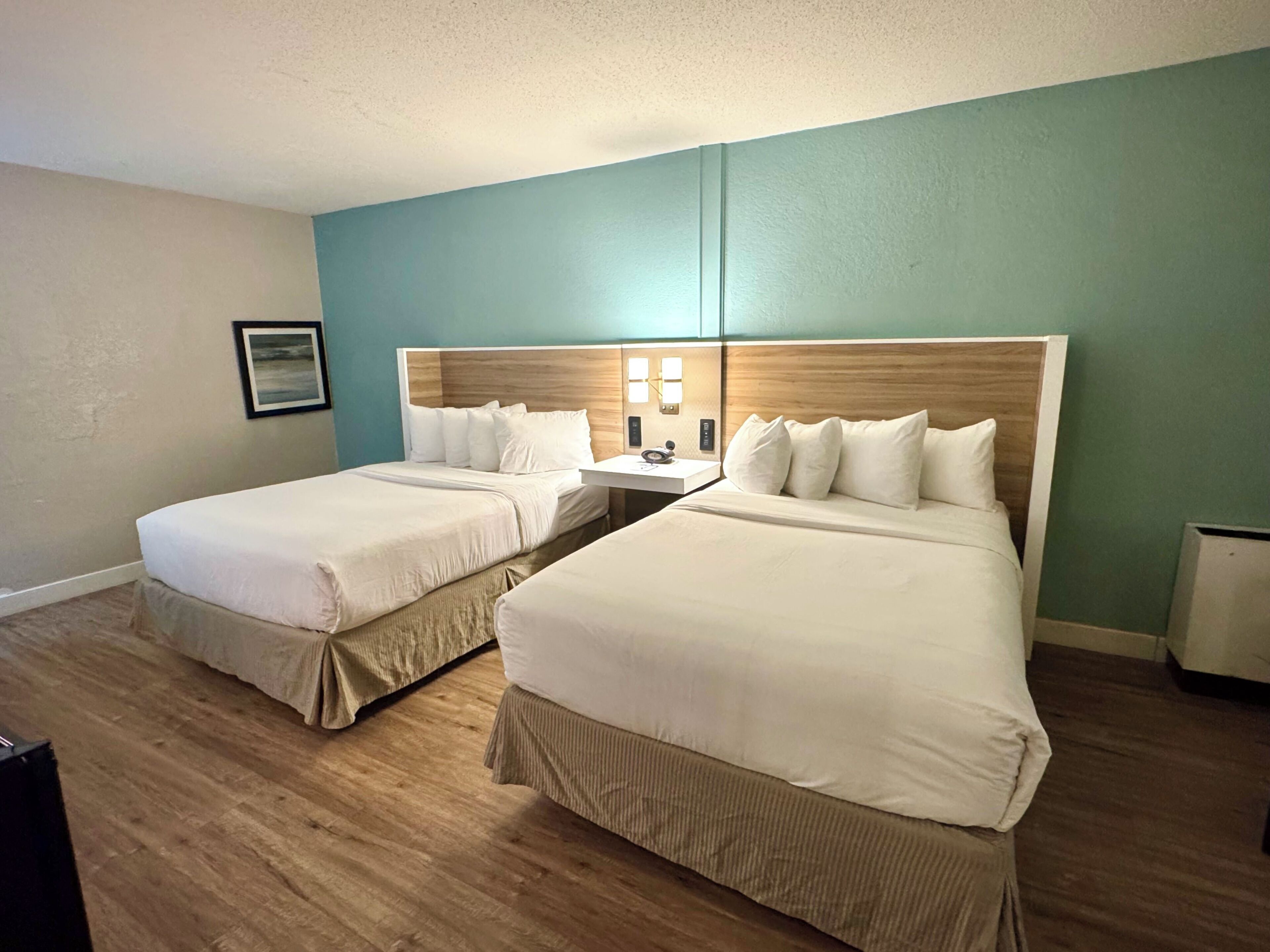 Habitación de hotel con dos camas, suelo de madera, una mesita de noche e iluminación en la pared.