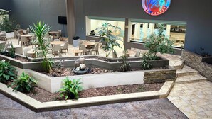 Un espace patio intérieur aménagé avec différents coins salon, une fontaine décorative et un panneau lumineux au néon sur le mur.