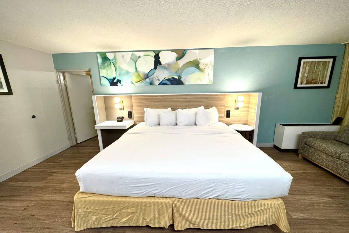 Ein Hotelzimmer mit einem großen Bett, einem Nachttisch, einer Lampe, einem Sofa und einem Bild an der Wand.