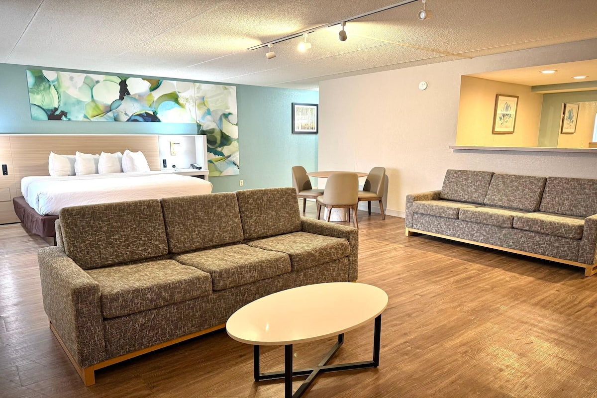 Ein modernes Hotelzimmer mit einem Bett, zwei Sofas, einem kleinen Tisch und einem großen, abstrakten Gemälde an der Wand.