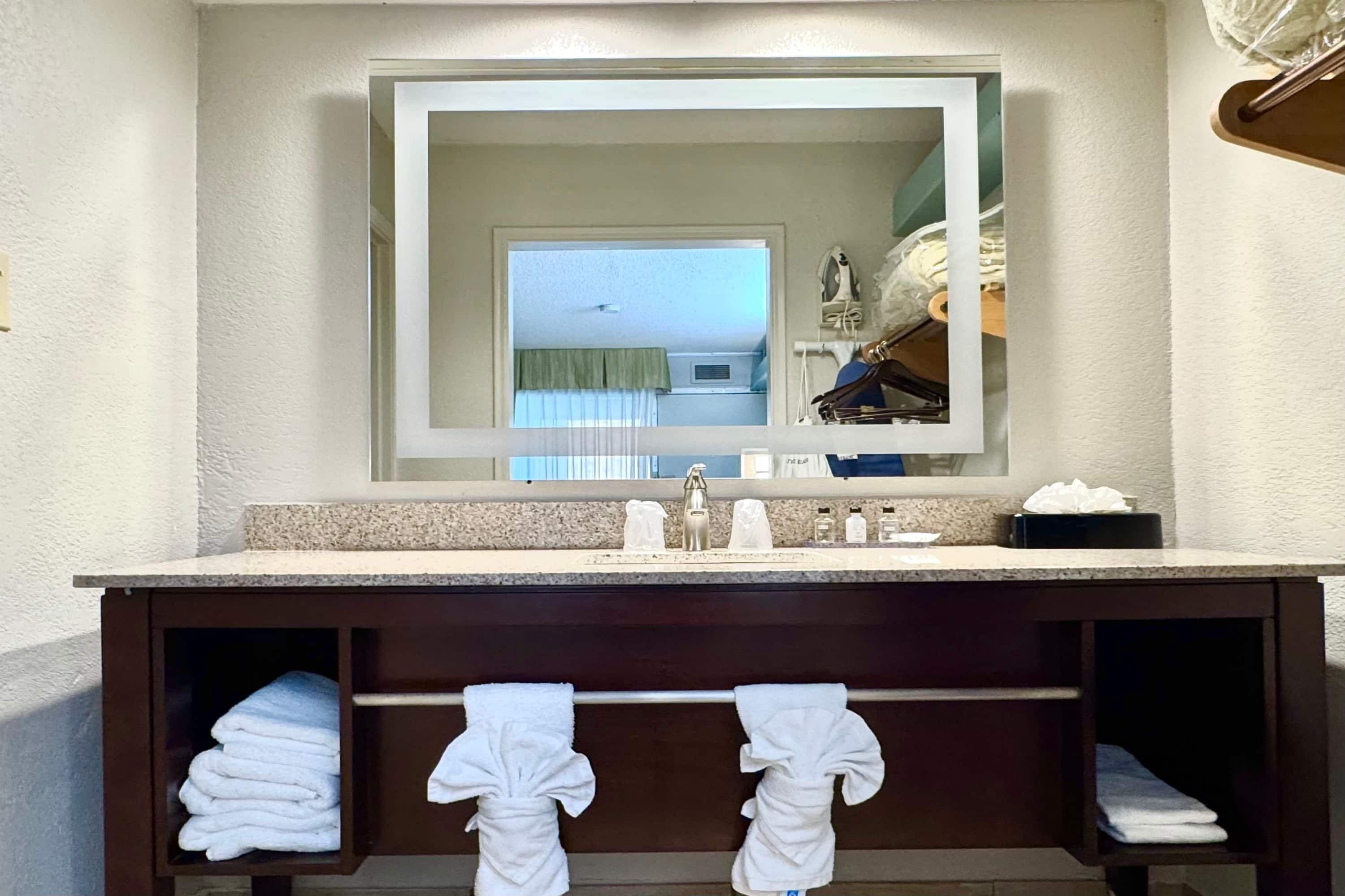 Une salle de bain avec un grand miroir, un lavabo et deux porte-serviettes sur lesquels sont pliées des serviettes.