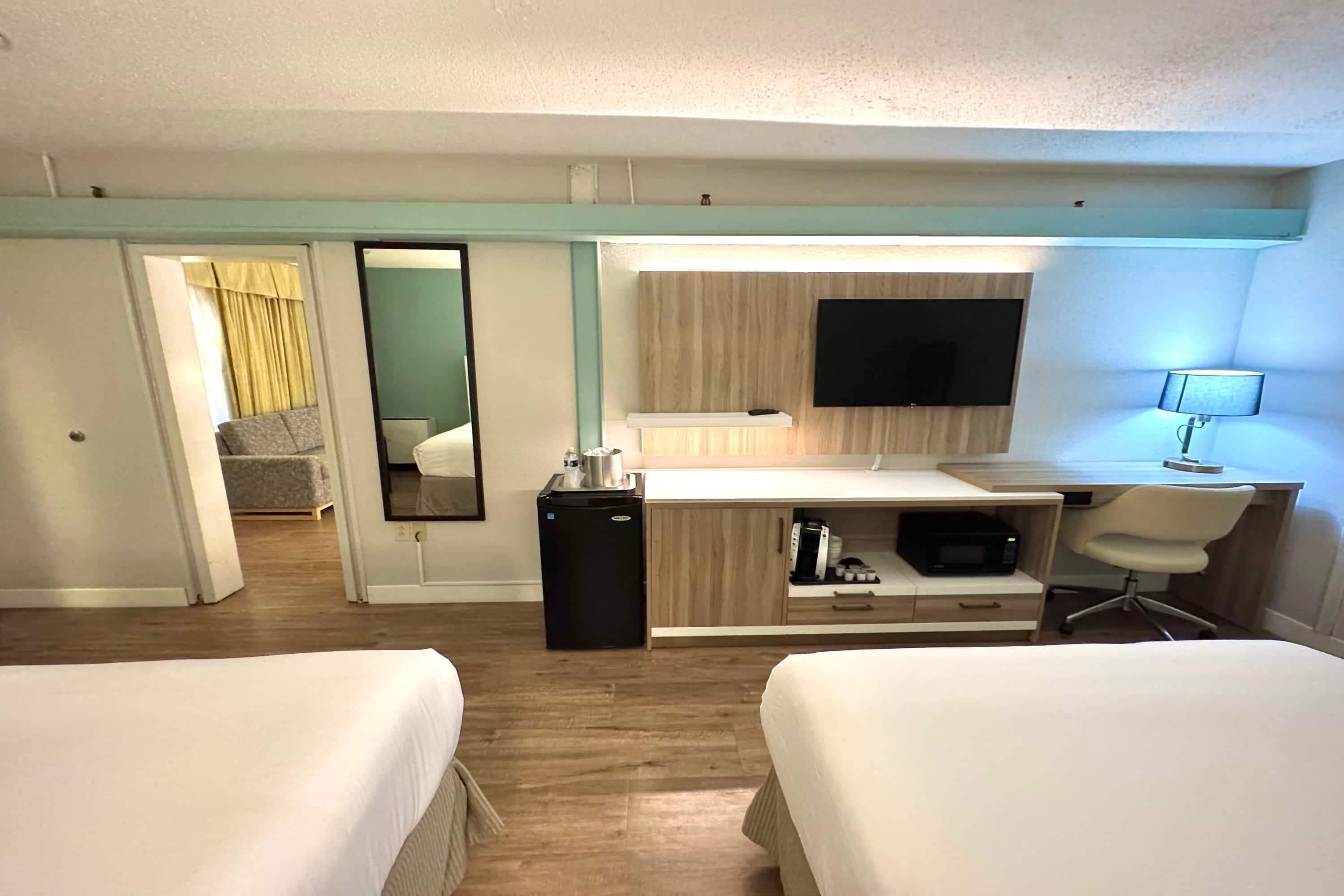 Une chambre d’hôtel avec deux lits, un bureau avec un ordinateur, une télévision et un petit réfrigérateur.