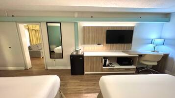 Une chambre d’hôtel avec deux lits, un bureau avec un ordinateur, une télévision et un petit réfrigérateur.