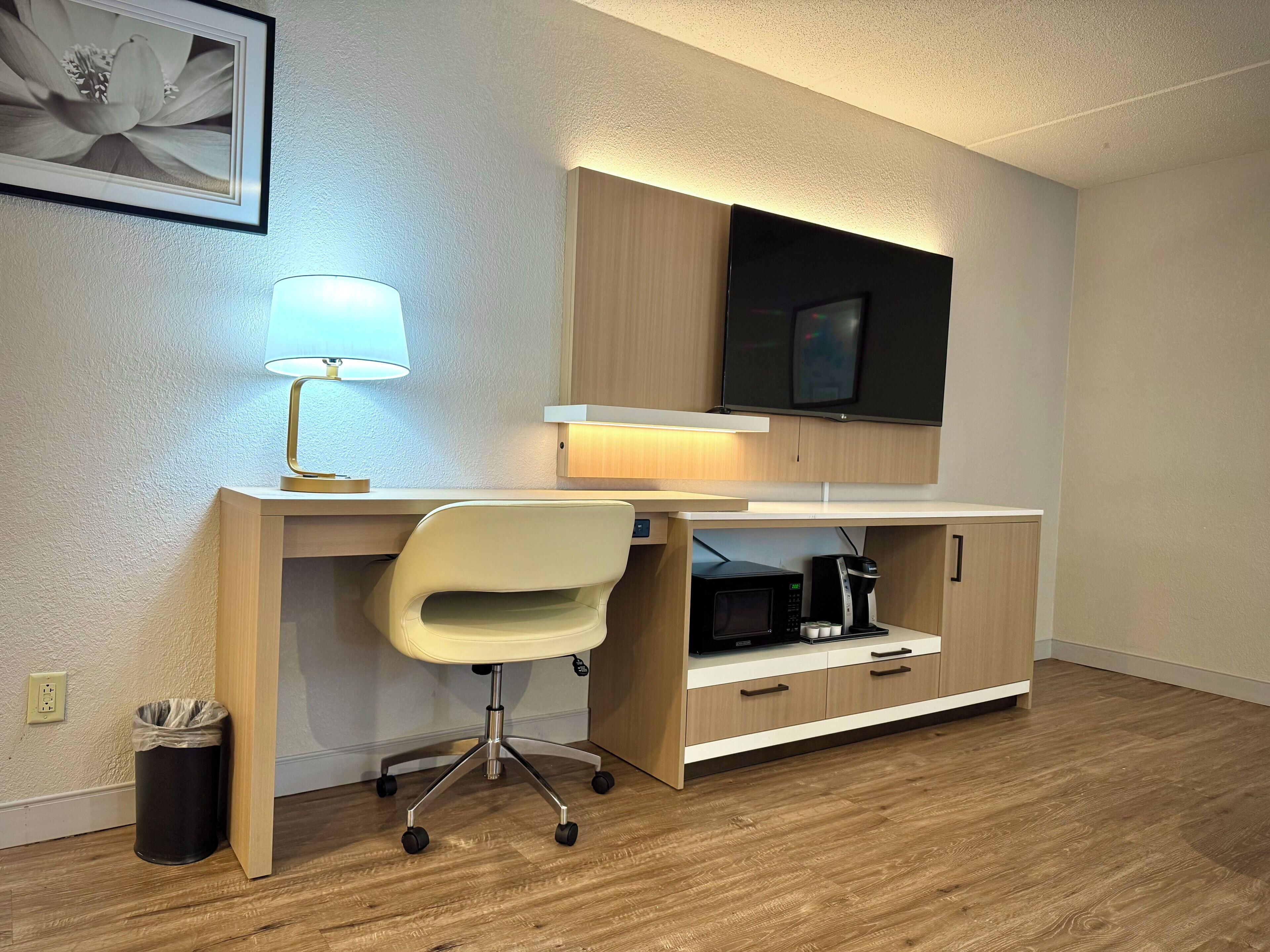 Quarto moderno com escrivaninha de madeira, uma cadeira, TV na parede, luminária e um cesto de lixo.