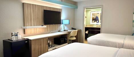 A hotel room with two beds, a desk with a computer, a TV, and a minibar.
