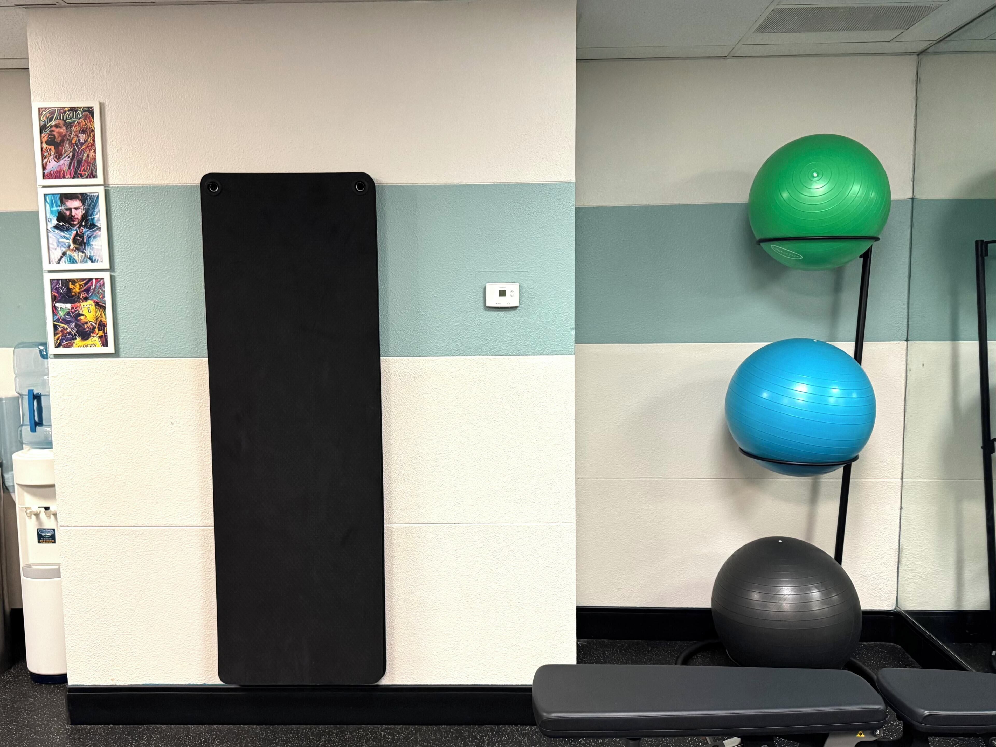 Un gimnasio con equipo de ejercicio, incluyendo una colchoneta negra, balones de ejercicio verde y azul, y un banco.
