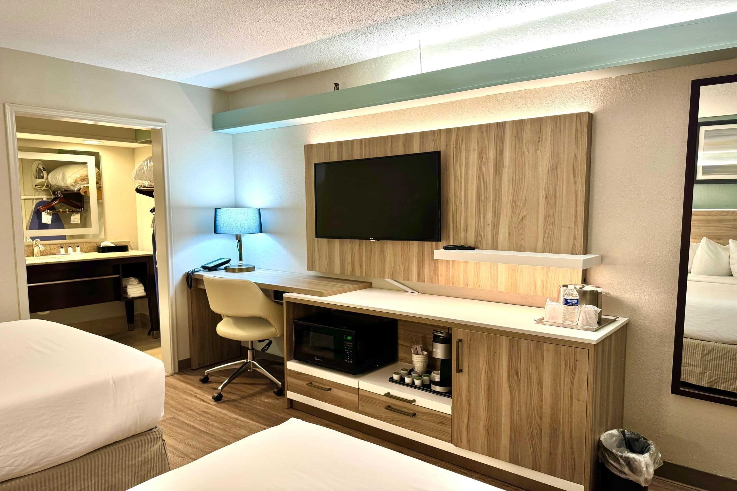 Una habitación de hotel con cama, escritorio, computadora, televisor y microondas.