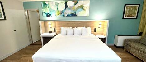 Una habitación de hotel con una cama grande, dos mesitas de noche, una obra de arte colgada en la pared y un sofá.