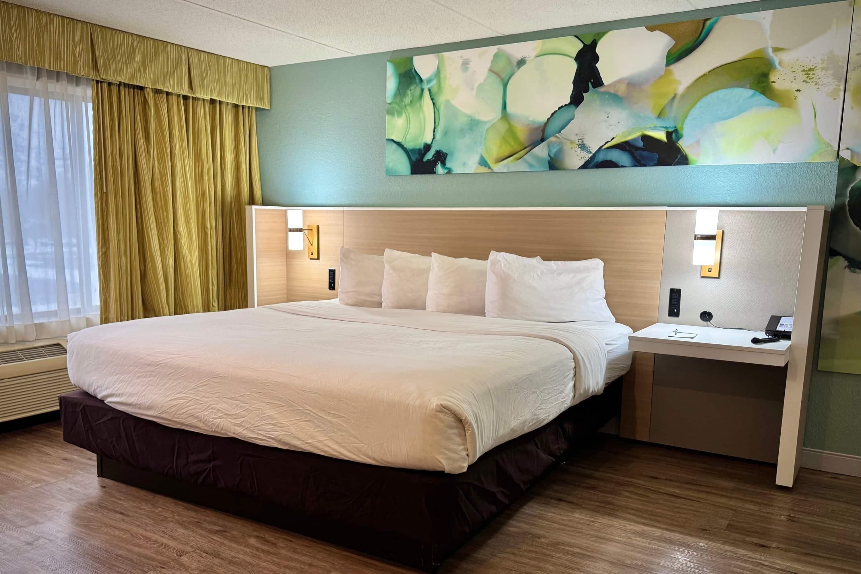 Habitació d'hotel amb un llit gran, una taula de nit amb un telèfon i un carregador, i una obra d'art penjada a la paret.