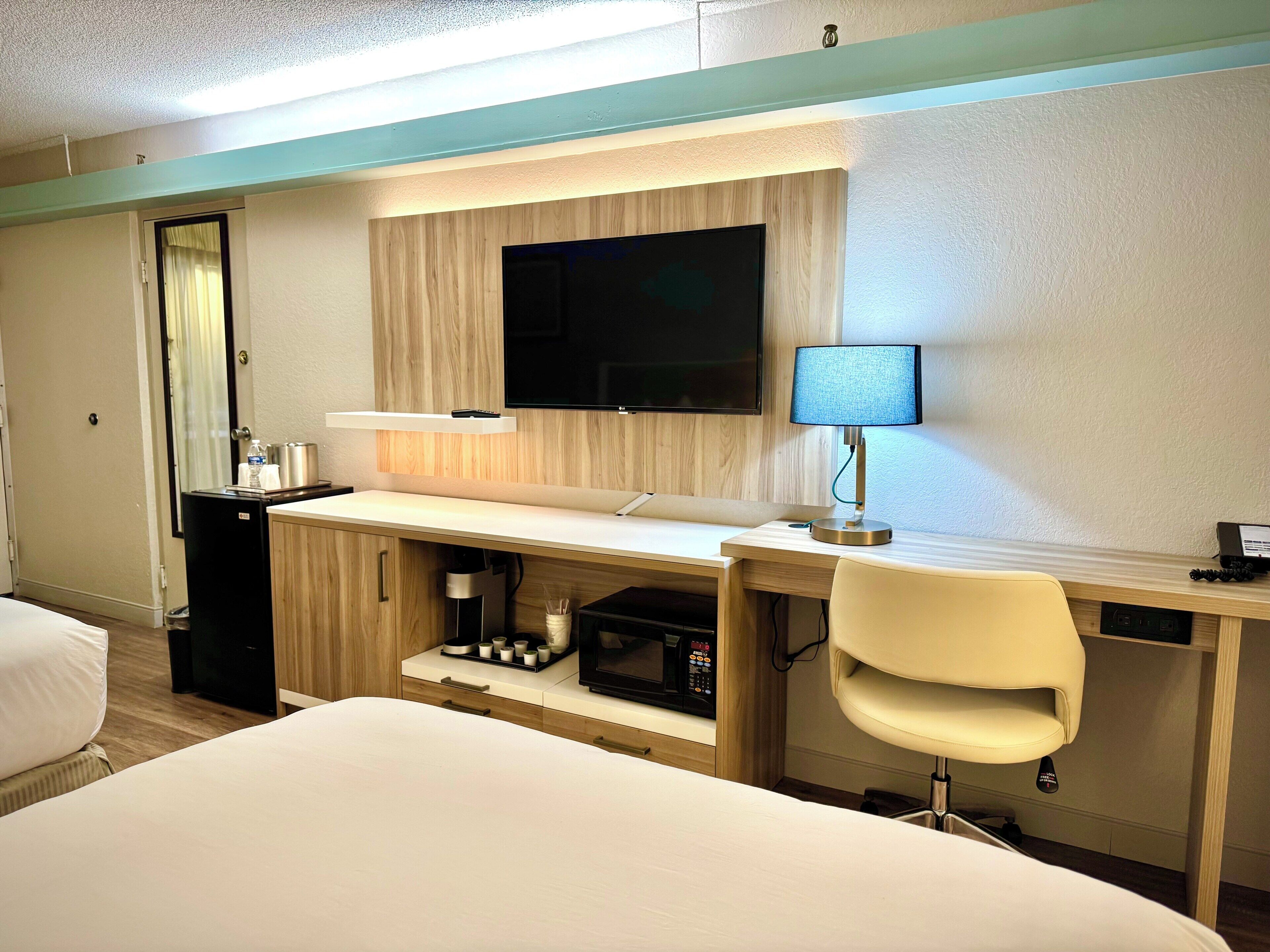 A hotel room with a bed, a desk with a lamp, a television, and a minibar.