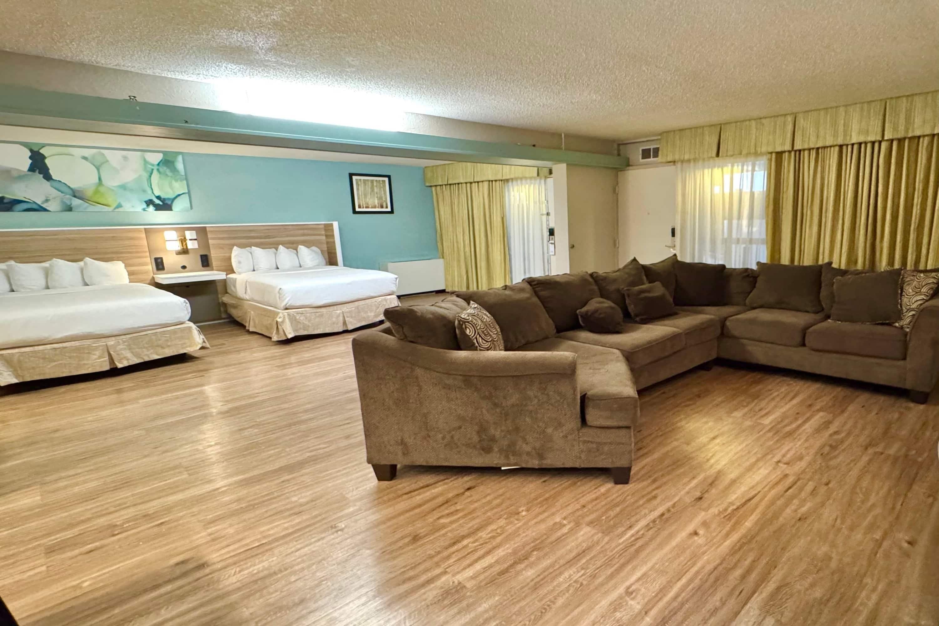A hotel room with two beds, a sofa, a wooden floor, and a painting on the wall.