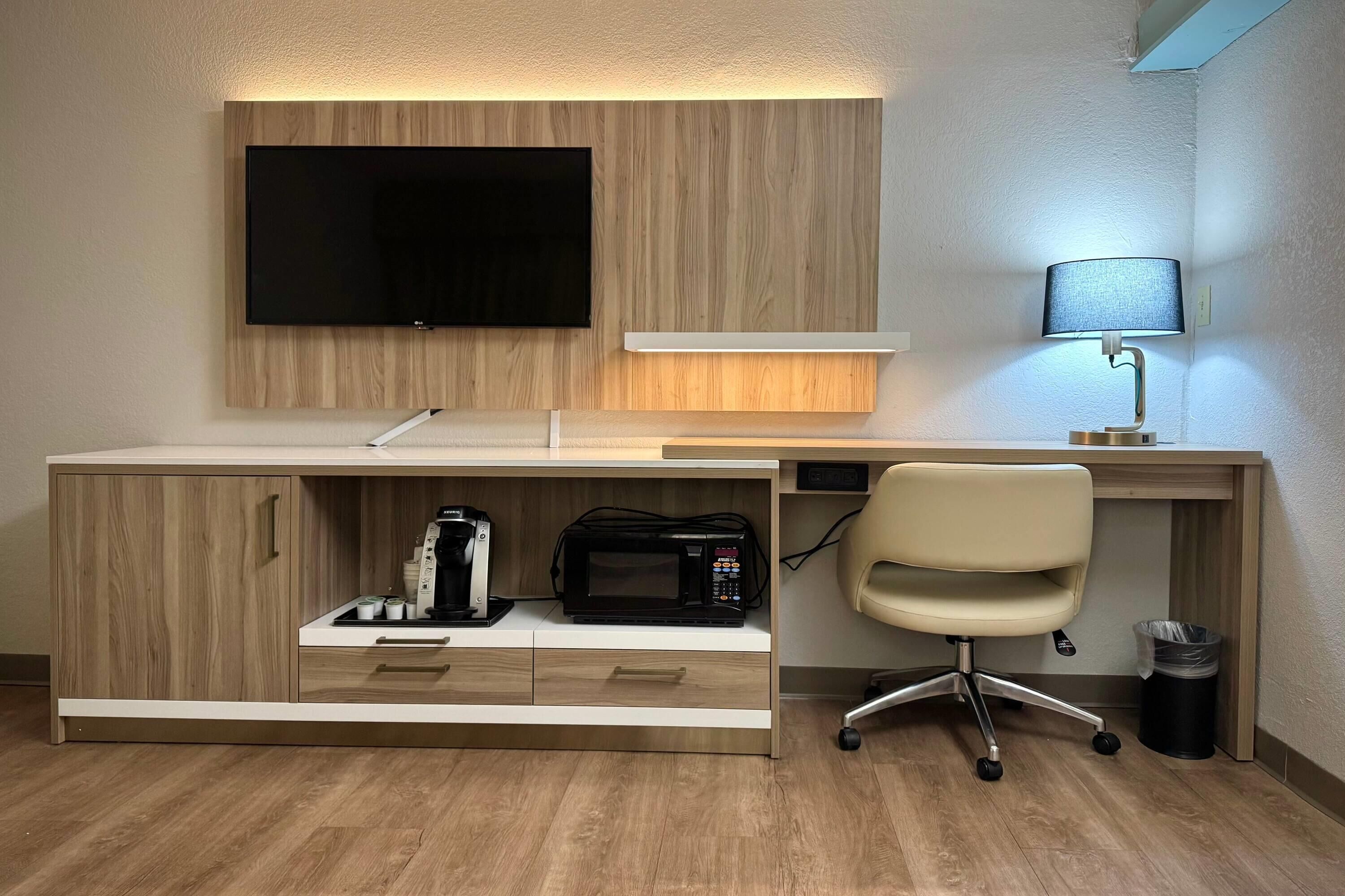 Un espace de bureau moderne avec un téléviseur à écran plat fixé à un mur en bois, un bureau avec une lampe, une chaise et une poubelle.