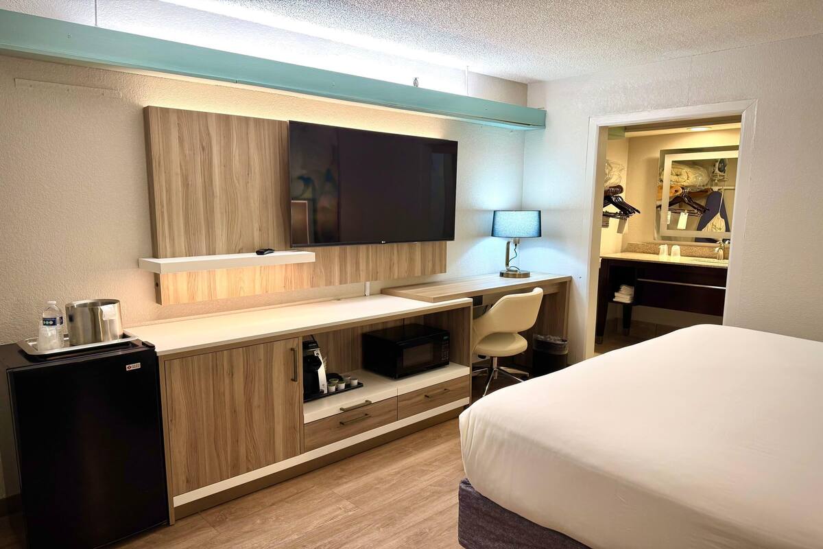Ein Hotelzimmer mit Bett, Schreibtisch mit Computer, Fernseher, kleinem Kühlschrank und angrenzendem Badezimmer.