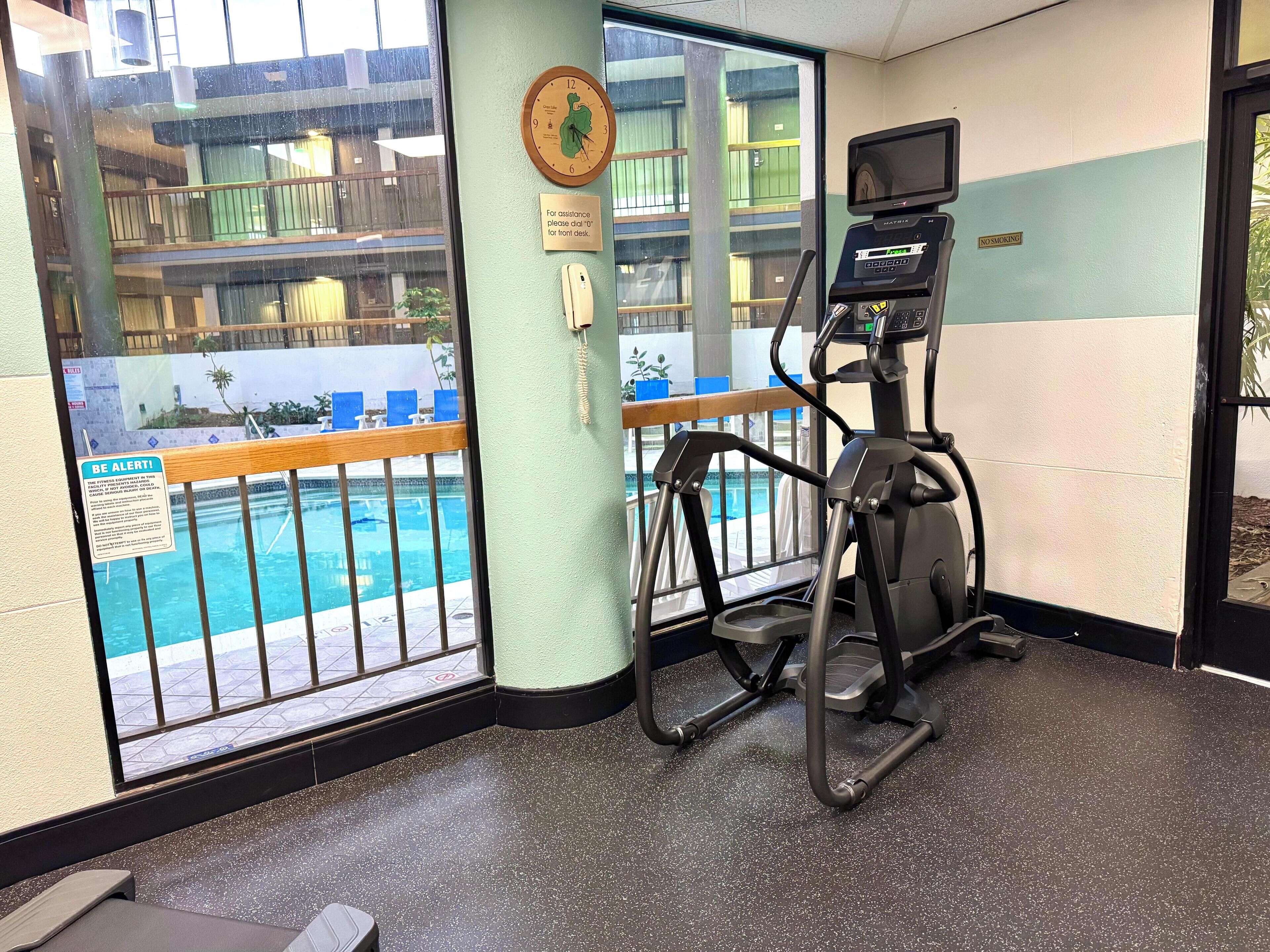 A fitness area with a treadmill, a pool view, and a sign for assistance.