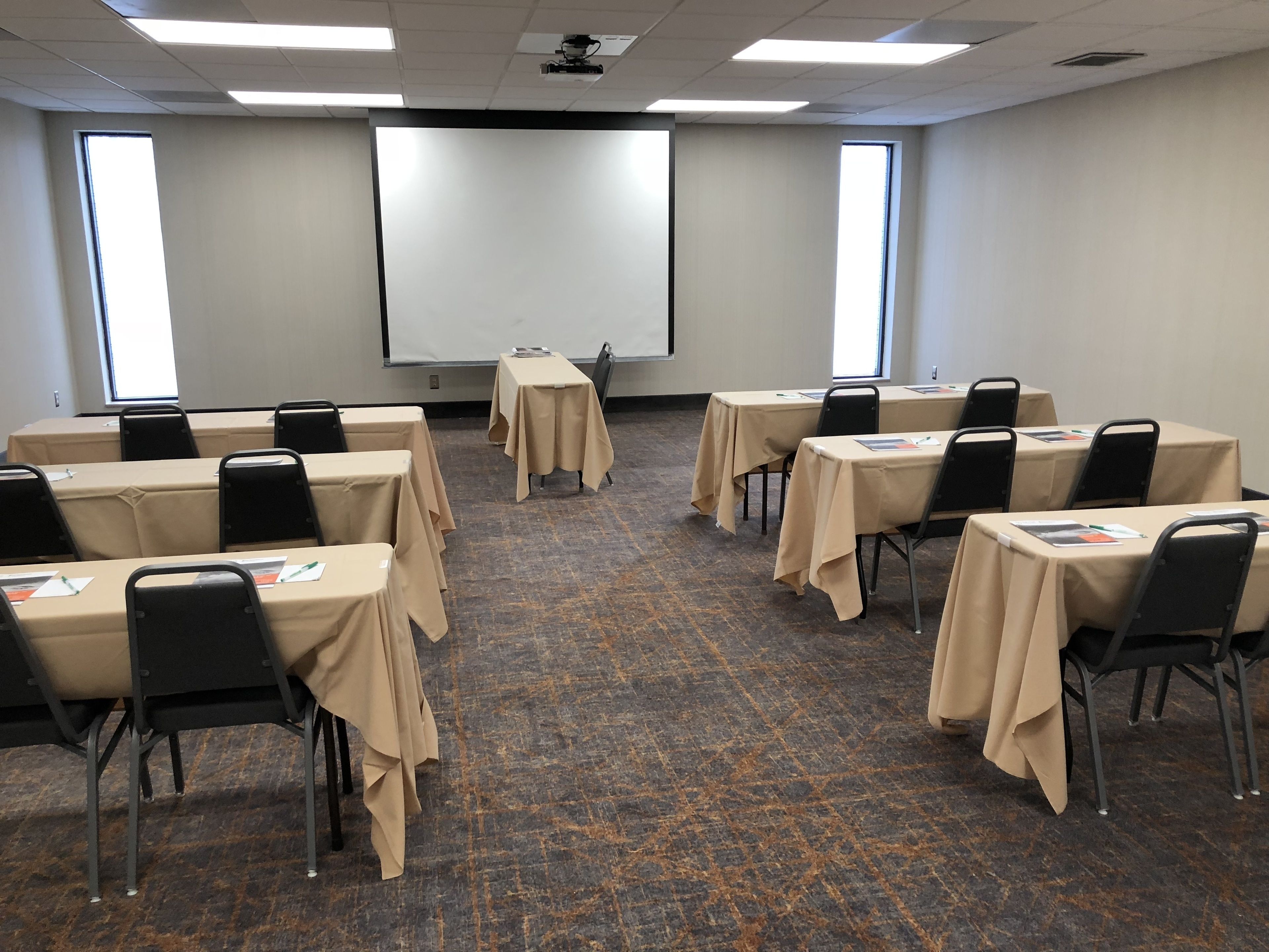 A conference room with tables and chairs, a projector screen, and windows.