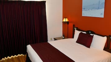 A hotel room with a large bed, a nightstand, a lamp, and a painting on the wall.