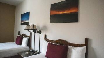 A hotel room with two beds, a nightstand, a lamp, and two paintings on the wall.