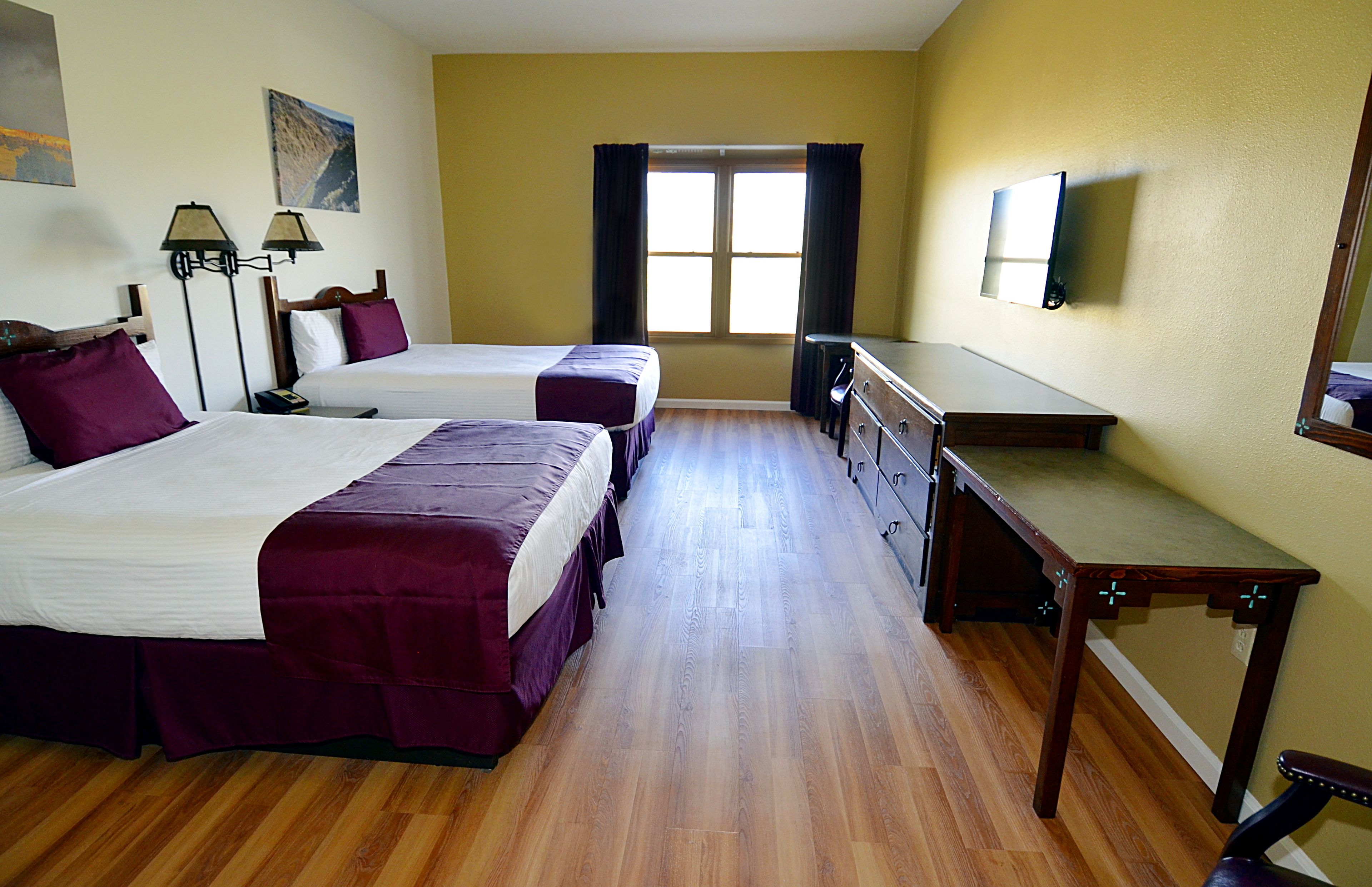 Habitación de hotel con dos camas, un escritorio, una cómoda y una ventana con cortinas.