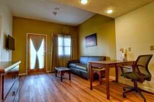 Uma sala de estar com sofá, mesa de madeira, televisão e uma porta com cortinas.