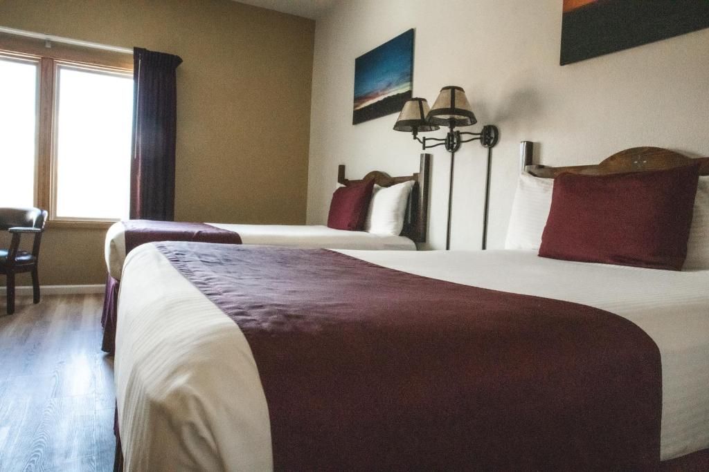 Habitación de hotel con dos camas, un escritorio, una silla, una lámpara y un cuadro en la pared.