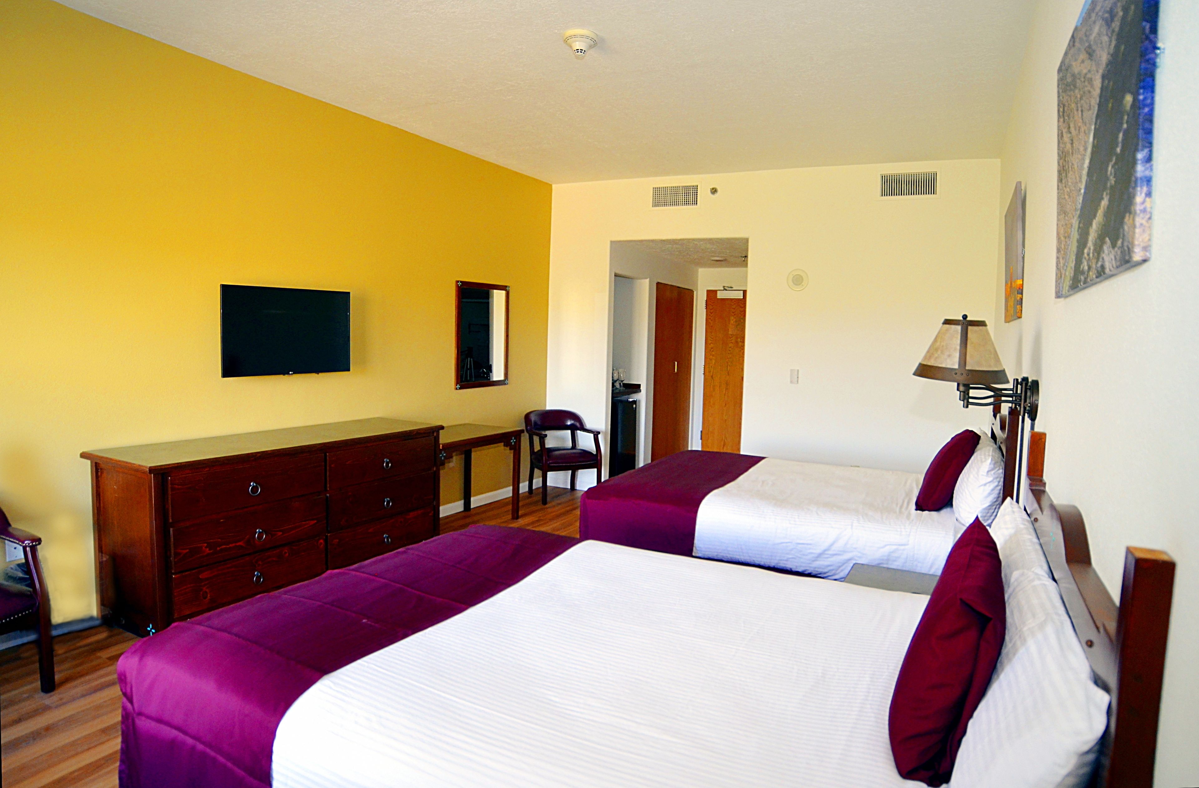 Una habitación de hotel con dos camas, un aparador de madera, una silla y un televisor en la pared.