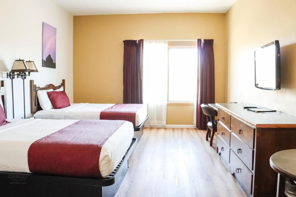 A hotel room with two beds, a desk, a chair, a TV, and a window with curtains.