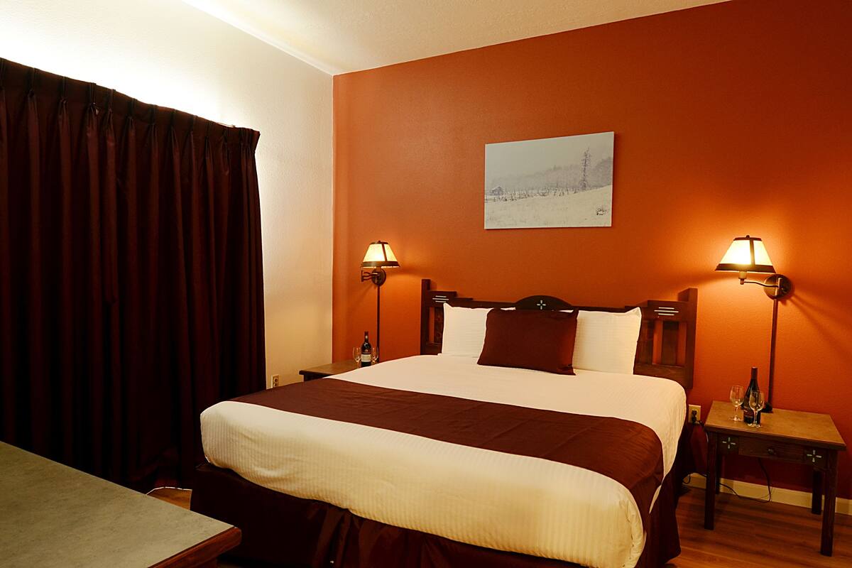 Un cuarto de hotel con una cama grande, dos mesitas de noche, una mesita auxiliar, una mesa de madera y un cuadro en la pared.