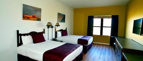 A hotel room with two beds, a television, a desk, and a window with curtains.