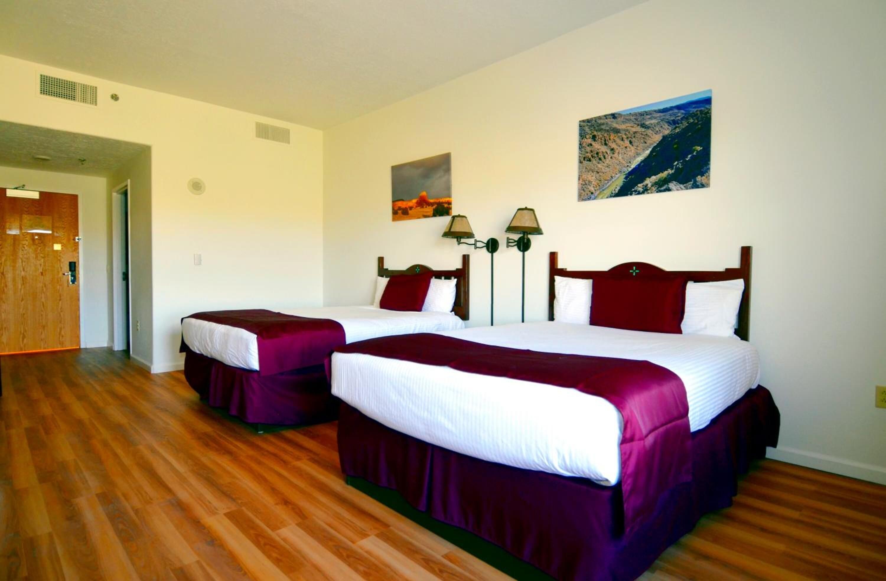 Habitación de hotel con dos camas, suelo de madera y un cuadro en la pared.