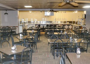 A restaurant with multiple tables and chairs, a kitchen area in the background, and ceiling fans. - Ohkay Casino Resort Hotel (Ohkay Owingeh)