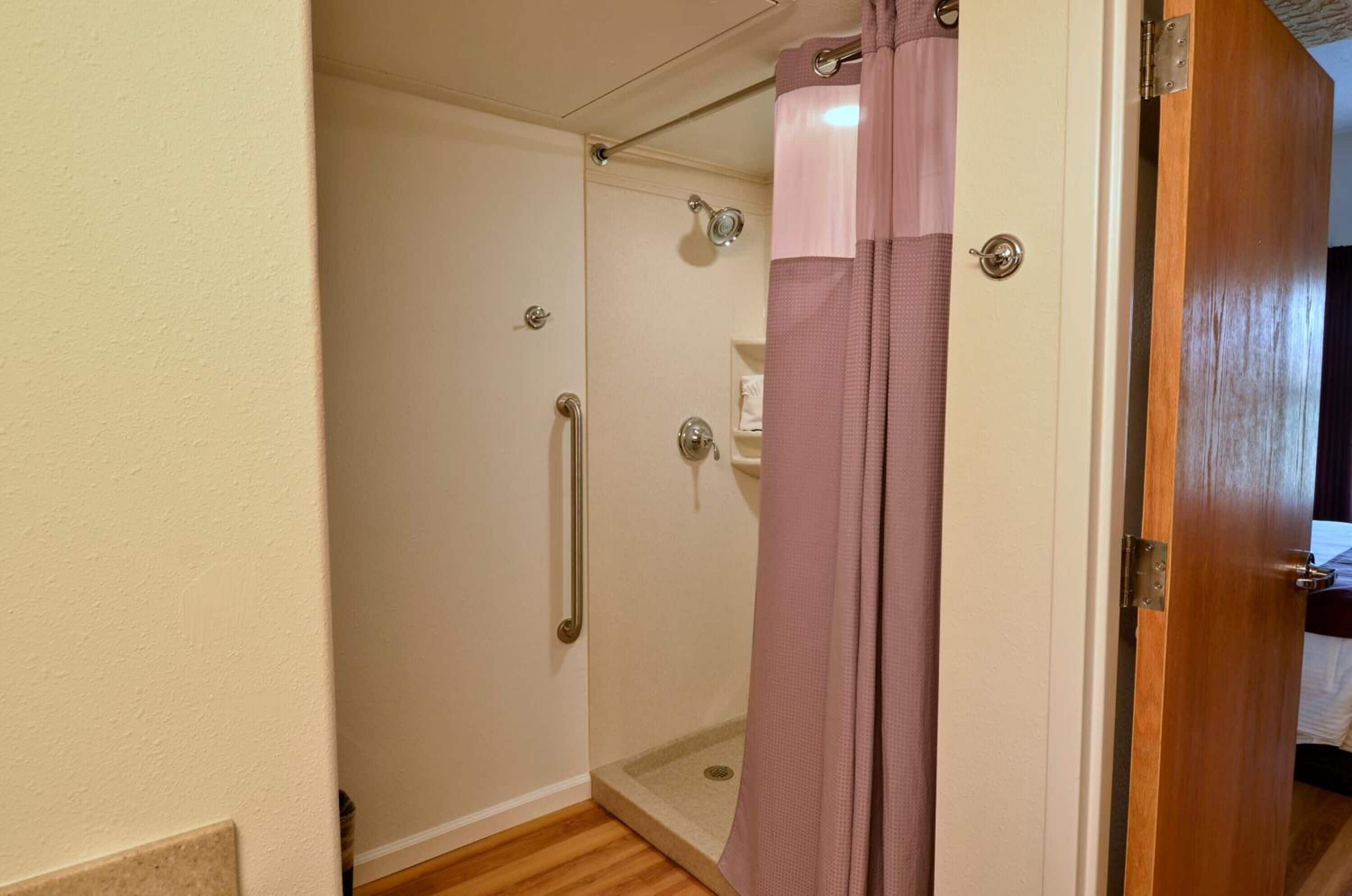 A shower with a glass door, a handrail, and a pink shower curtain.
