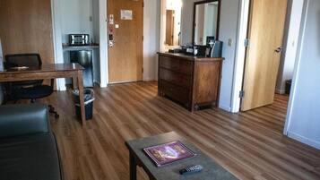 Un salon avec un plancher en bois, une table à manger avec des chaises, un coin cuisine avec un four à micro-ondes, une commode en bois et une porte avec un miroir.
