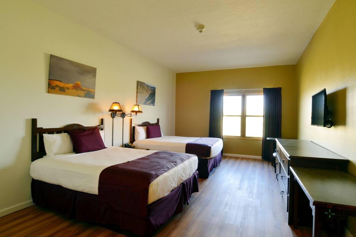 Una habitación de hotel con dos camas, un escritorio, un televisor y obras de arte en las paredes.