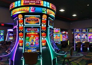 A casino slot machine area with multiple machines, chairs, and a carpeted floor. - Ohkay Casino Resort Hotel (Ohkay Owingeh)