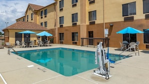A hotel pool area with a clear pool, lounge chairs, and umbrellas.