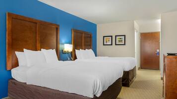 A hotel room with two beds, a wooden headboard, a nightstand, a lamp, and a door.