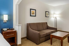 A hotel room with a brown sofa, a wooden nightstand with a phone, a lamp, and two framed pictures on the wall. - Comfort Inn Garner Clayton I-40 (Garner)