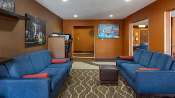 Un hall de hotel con dos sofás azules, un mostrador de recepción y un cuadro con una vista de la ciudad.