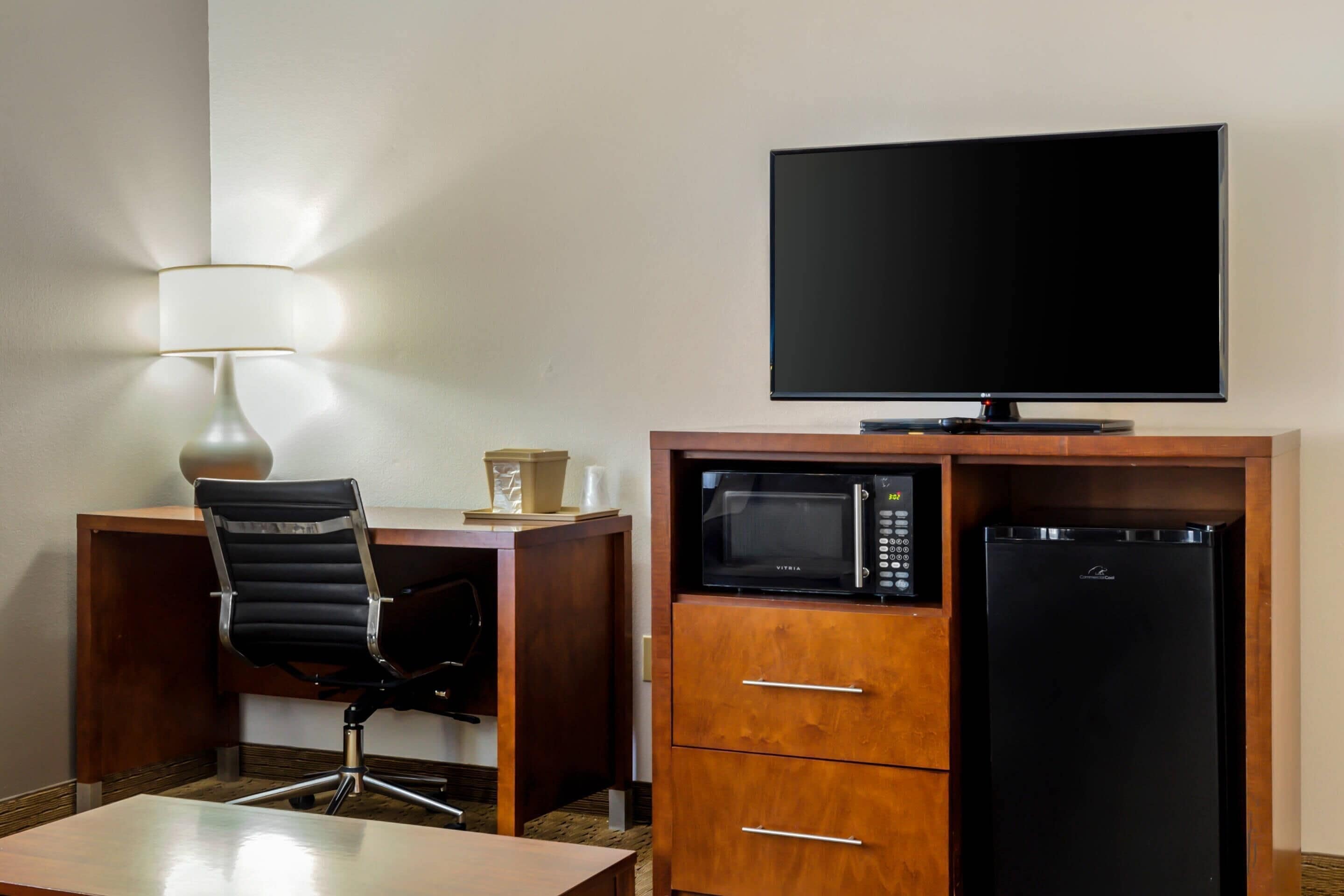Ein Hotelzimmer mit Schreibtisch, Stuhl, Flachbildfernseher, Mikrowelle und Kühlschrank.