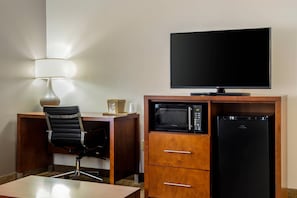 A hotel room with a desk, a chair, a flat-screen TV, a microwave, and a refrigerator.