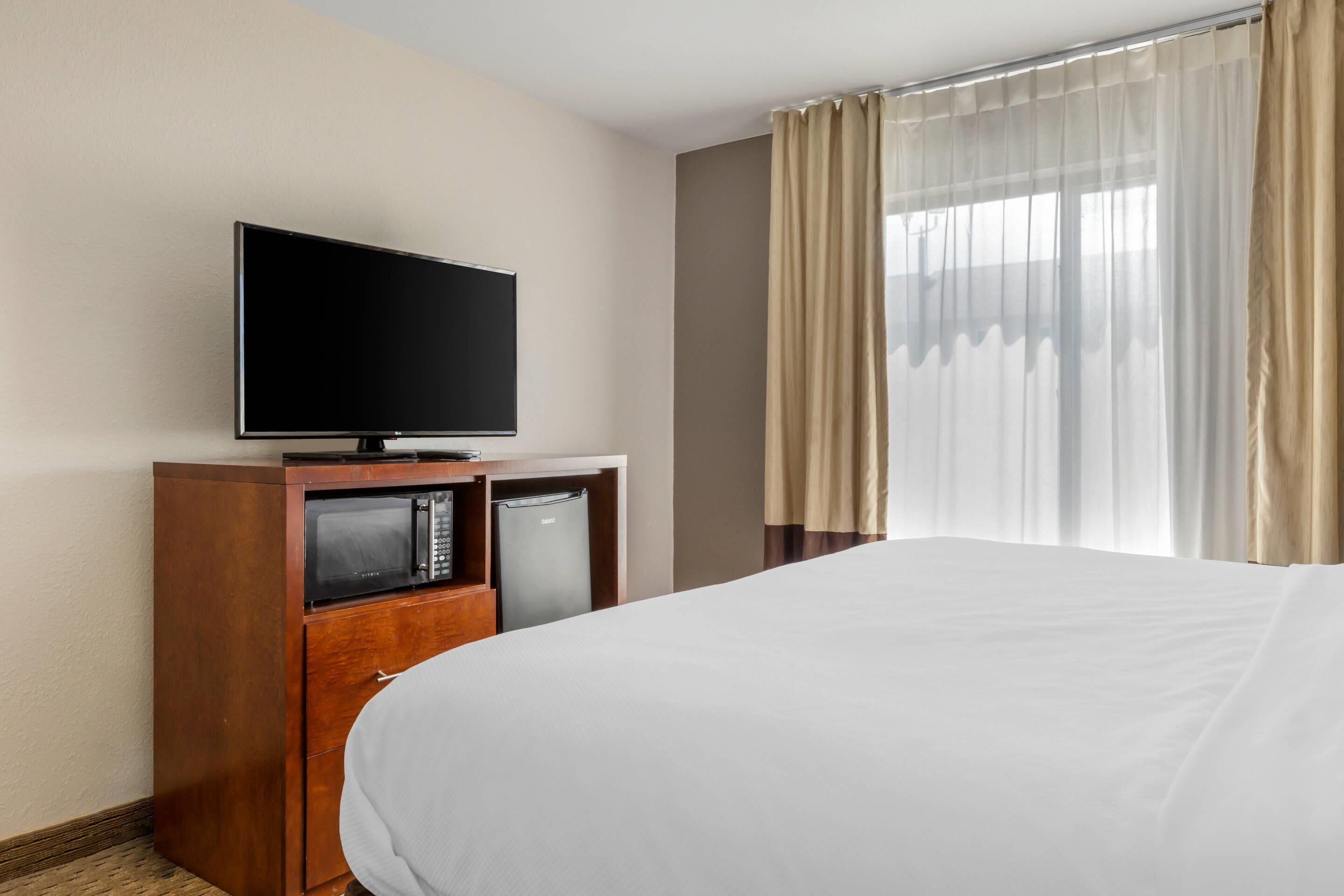 Habitación de hotel con una cama, un televisor sobre un soporte de madera, un microondas y un refrigerador.