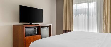 Habitación de hotel con una cama, un televisor sobre un soporte de madera, un microondas y un refrigerador.