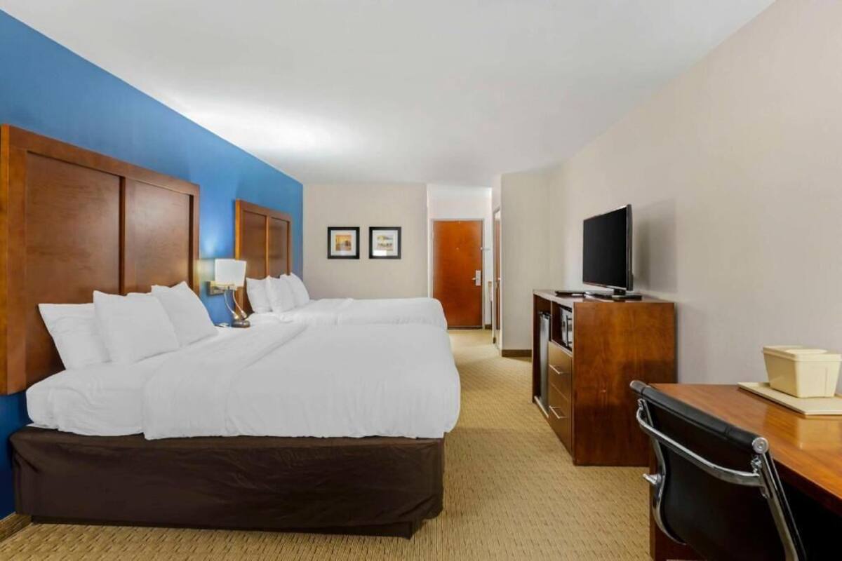 A hotel room with a large bed, a desk with a chair, a television, and a minibar.