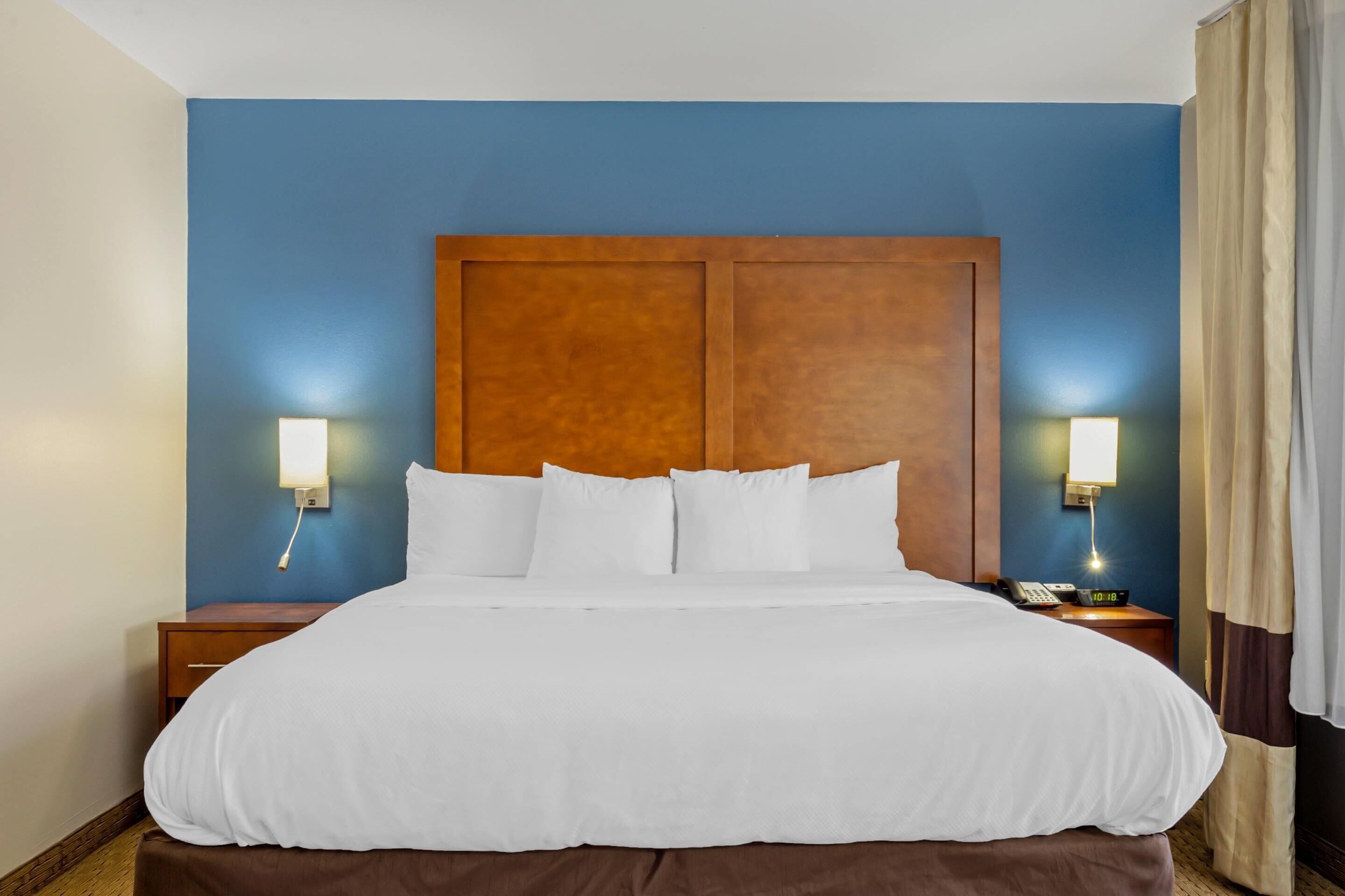 A hotel room with a large bed, two bedside tables, a wooden headboard, and two wall-mounted lamps.