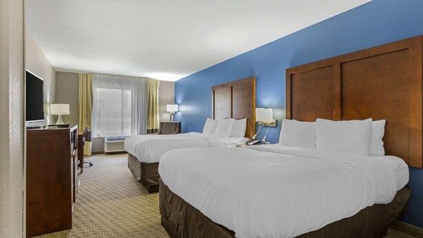 A hotel room with two beds, a TV, a desk, and a window with curtains.