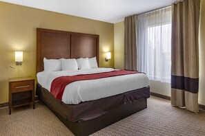 A hotel room with a large bed, two bedside tables, a wooden headboard, and a window with curtains. - Comfort Inn Garner Clayton I-40 (Garner)